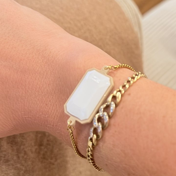 A TapLoop bracelet with a white stone on a gold chain, worn on a wrist beside a gold link bracelet